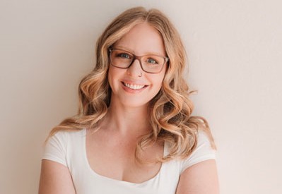 Emily standing with arms crossed, smiling in a white shirt