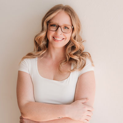 Emily standing with arms crossed, smiling in a white shirt