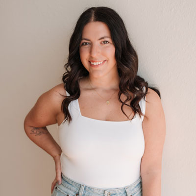 Maddie standing in a white tank top with her hand on her hip