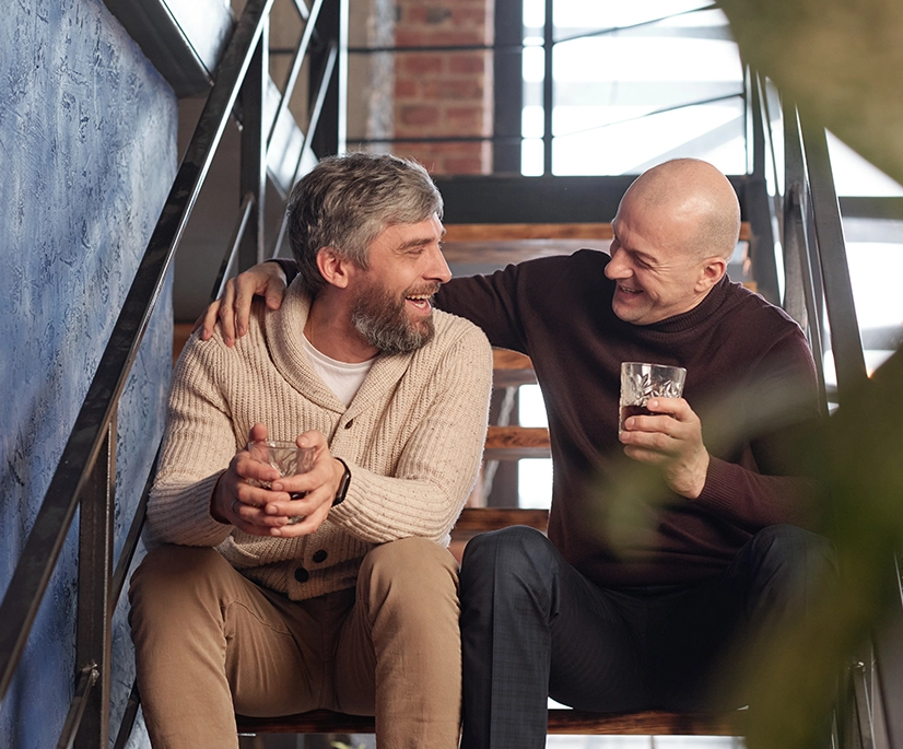 cheerful excited middle aged men sitting stairs drinking whisky while having fun